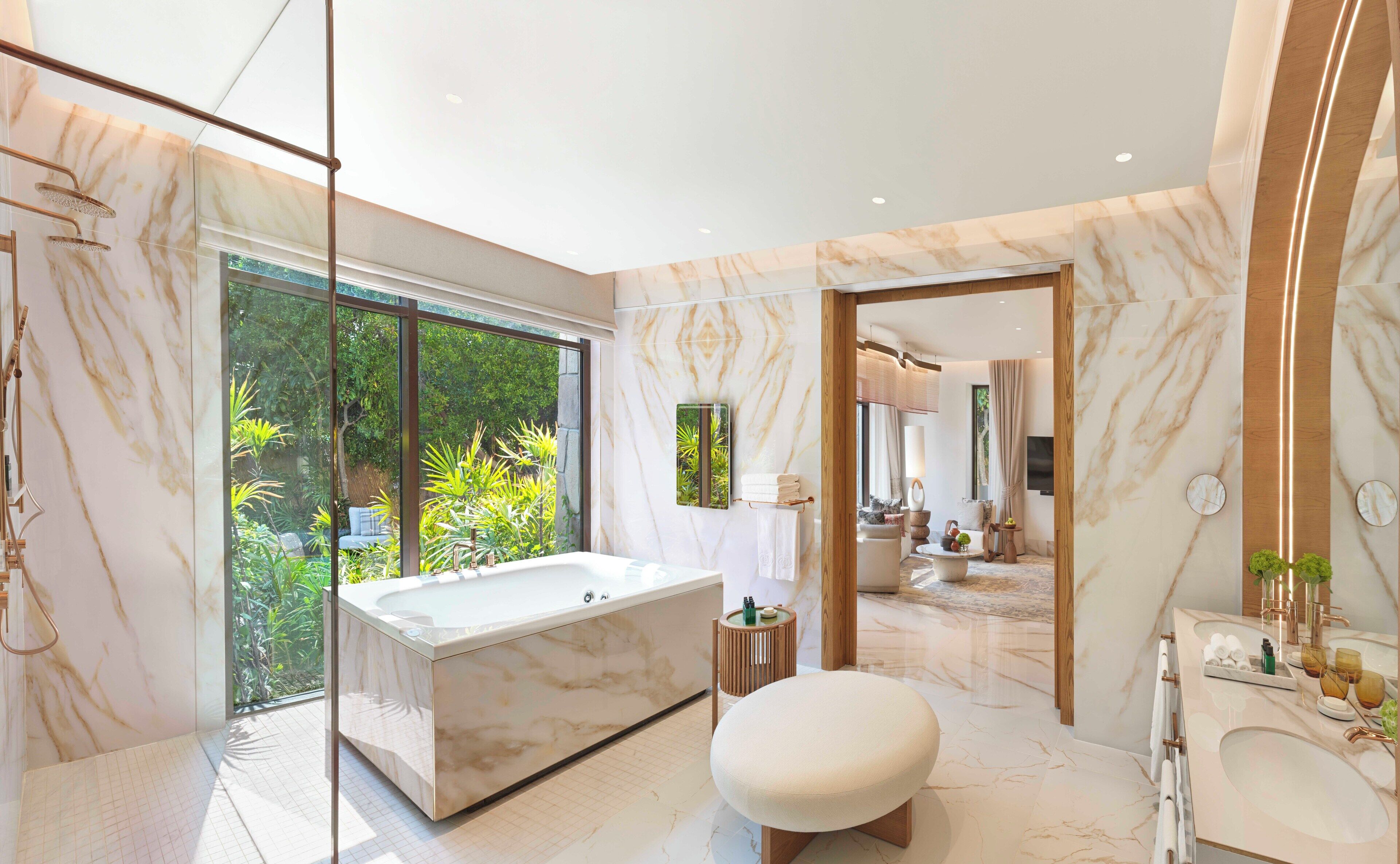A modern bathroom with a large bathtub, a round stool, and a vanity with a mirror.