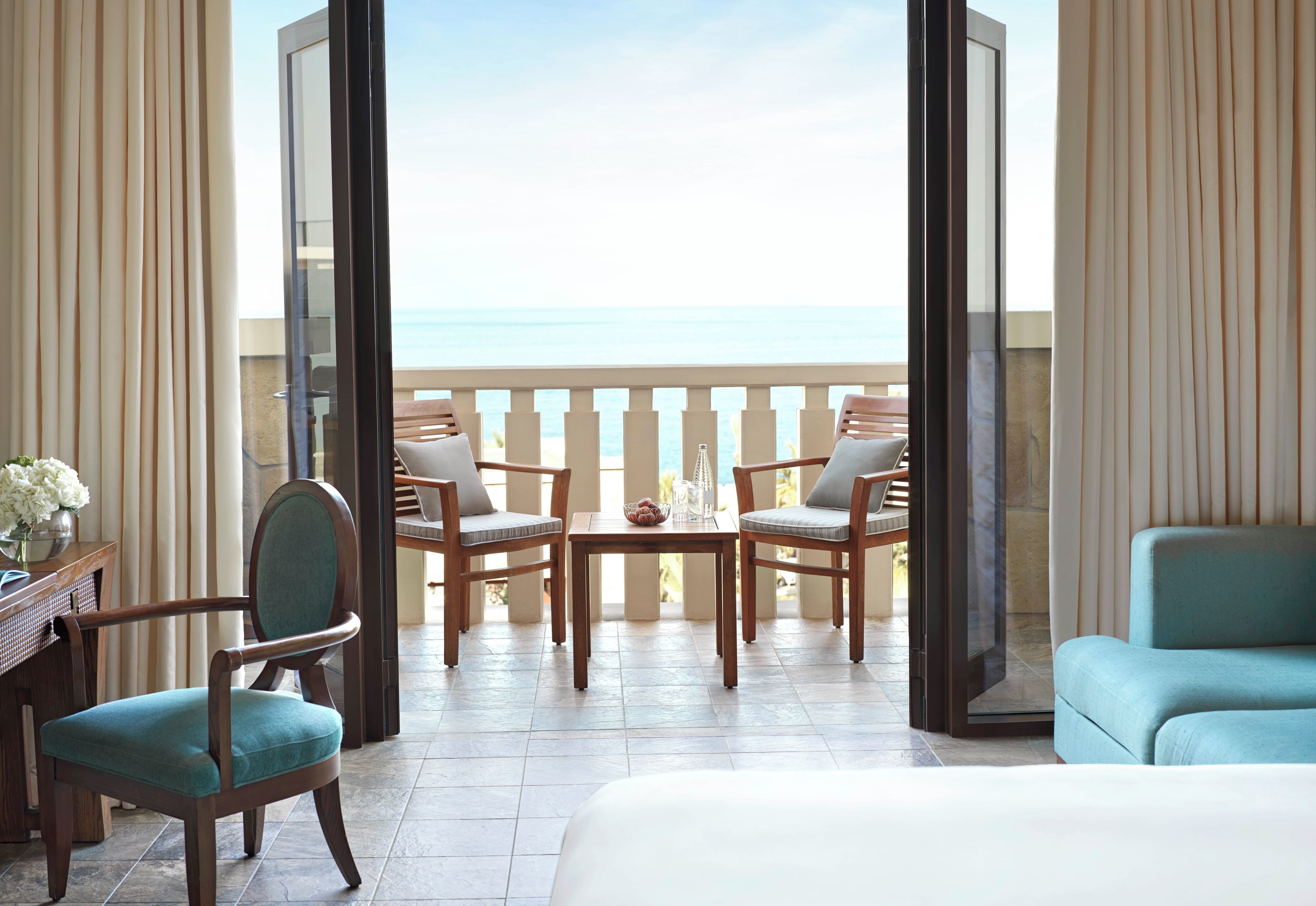 A balcony with a view of the sea, furnished with a table, chairs, and a sofa.