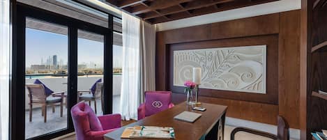 A modern hotel room with a wooden ceiling, a large window with a city view, a dining area with a wooden table, and a decorative wall panel.