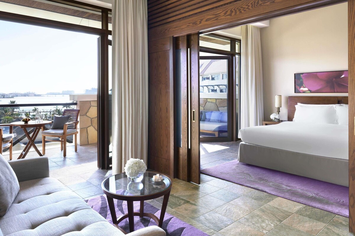 Een hotelkamer met balkon, een bed, een zithoek met tafel en uitzicht op de stad.
