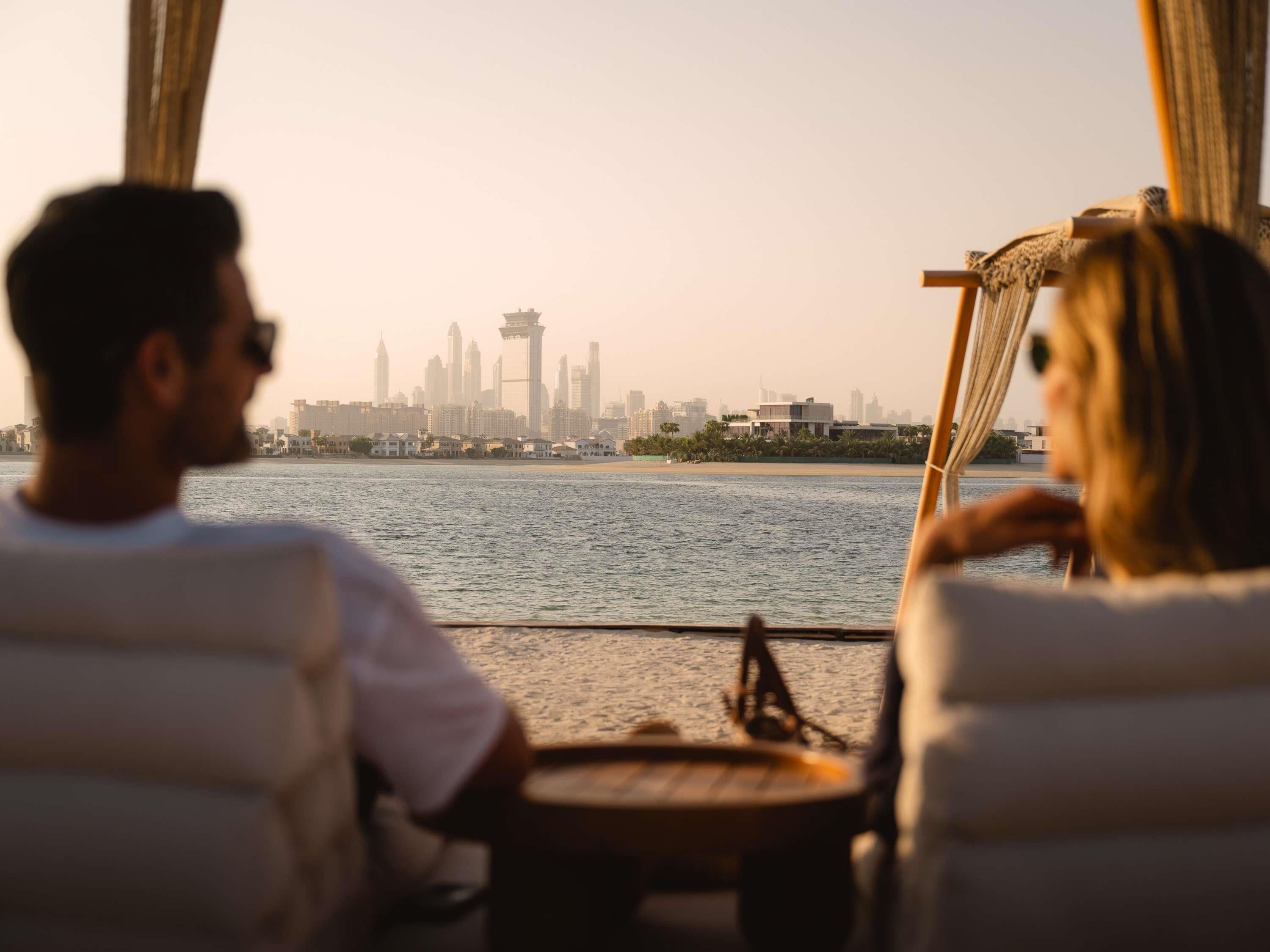 A couple seated at a table by a window overlooking a city skyline and water.
