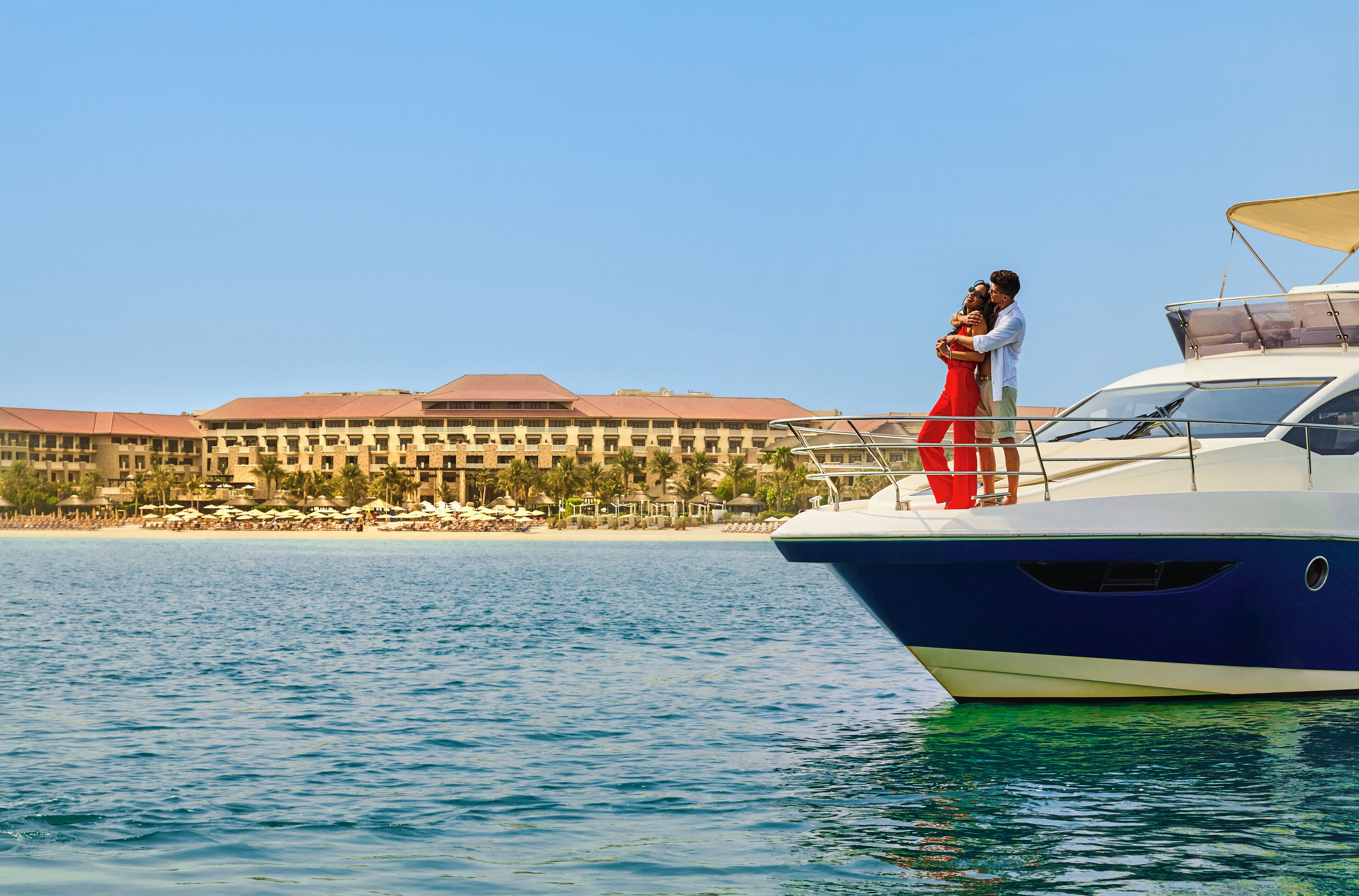 A couple embracing on a yacht with a resort in the background.