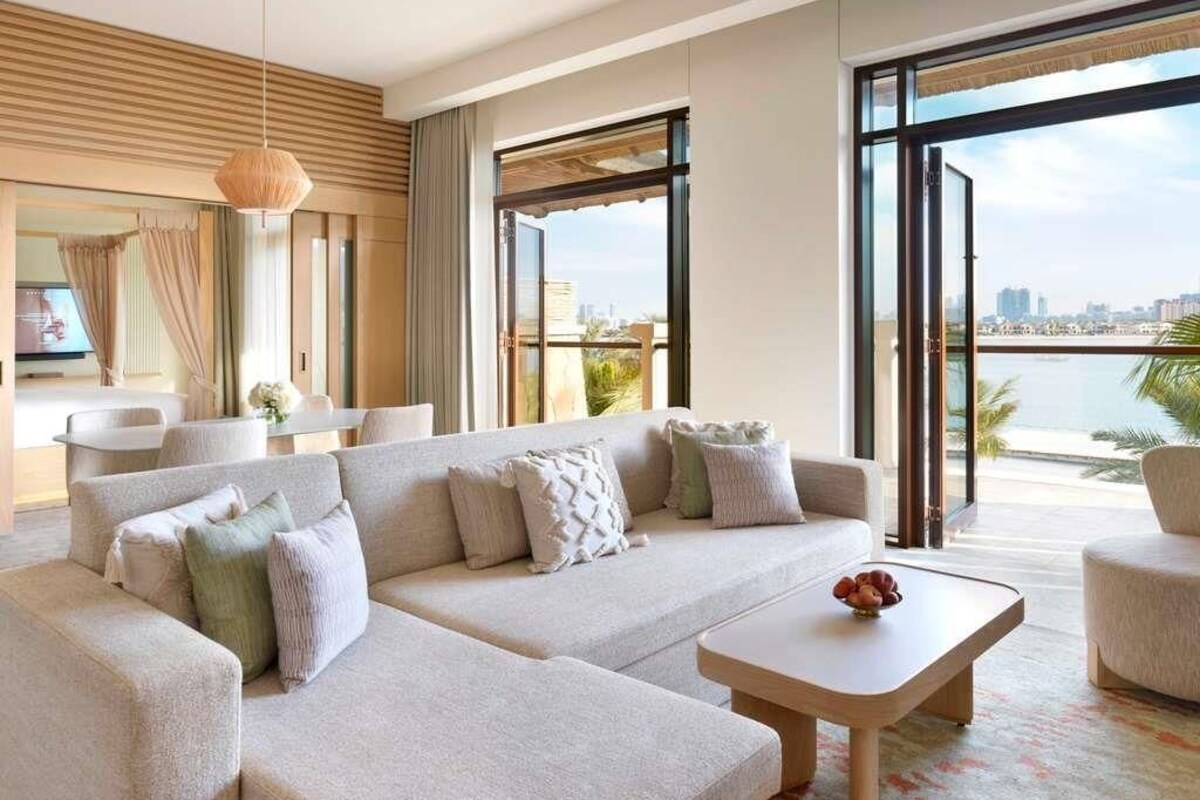 A modern living room with a sectional sofa, a coffee table, and large windows offering a view of a cityscape and water.
