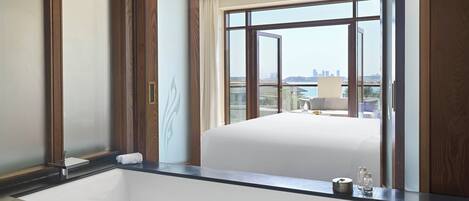 A hotel room with a large window, a white bed, a black countertop, and a sink.