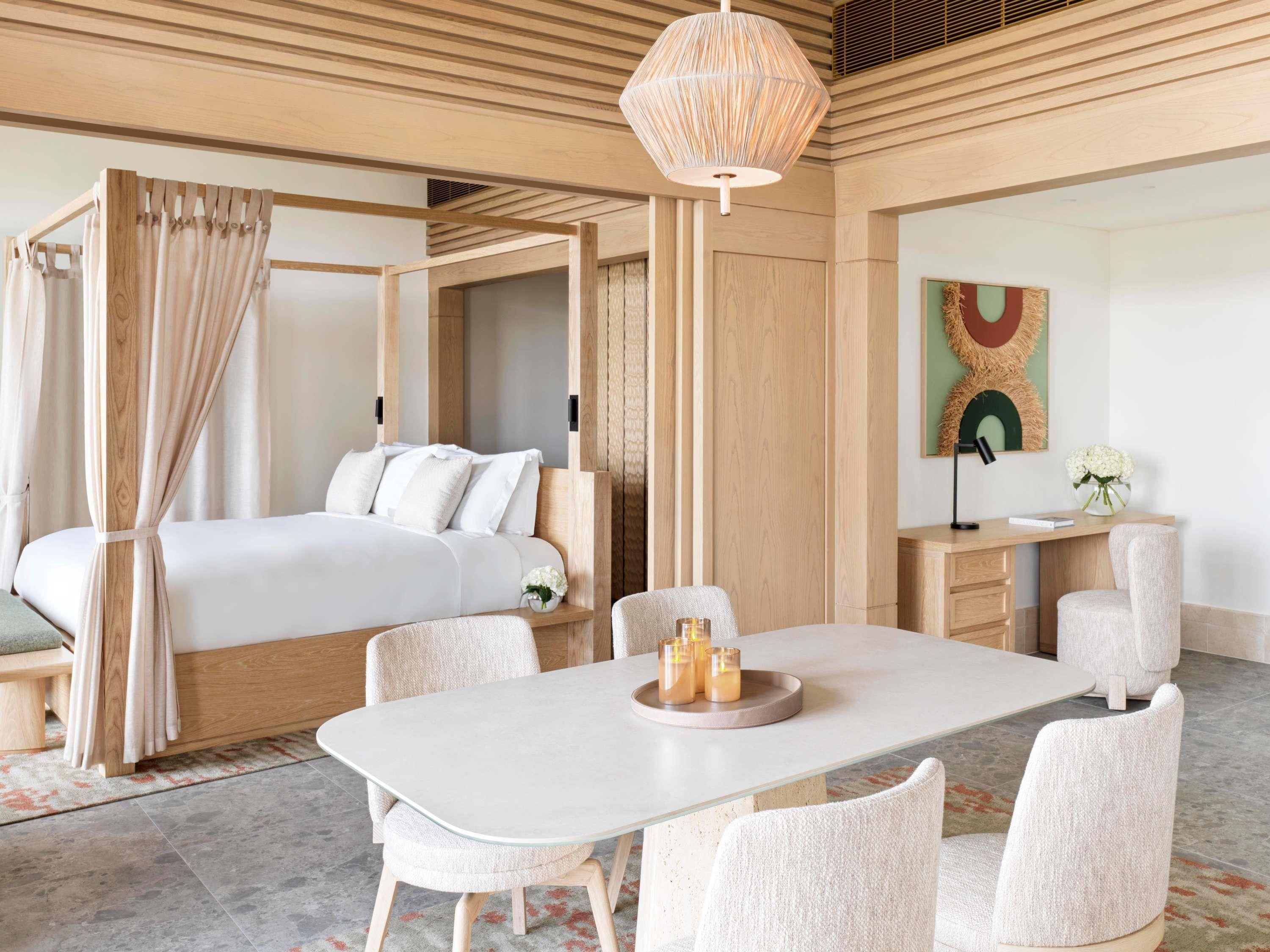 Una habitación de hotel moderna con una cama con dosel, una mesa de comedor con sillas, un escritorio con una silla y un gran ventanal.
