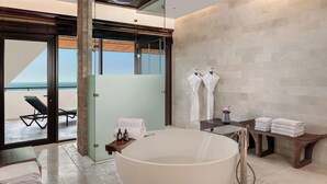A modern bathroom with a large bathtub, a glass shower enclosure, and a view of the beach.