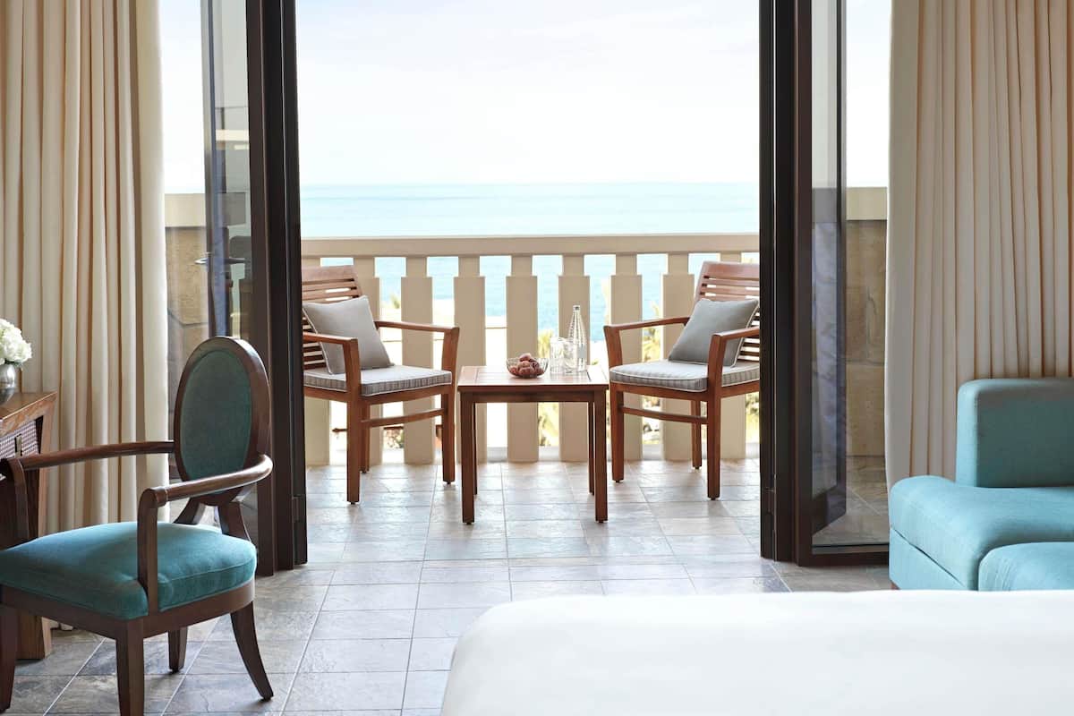 Een balkon met uitzicht op zee, voorzien van houten stoelen en een tafel, en een bed op de voorgrond.