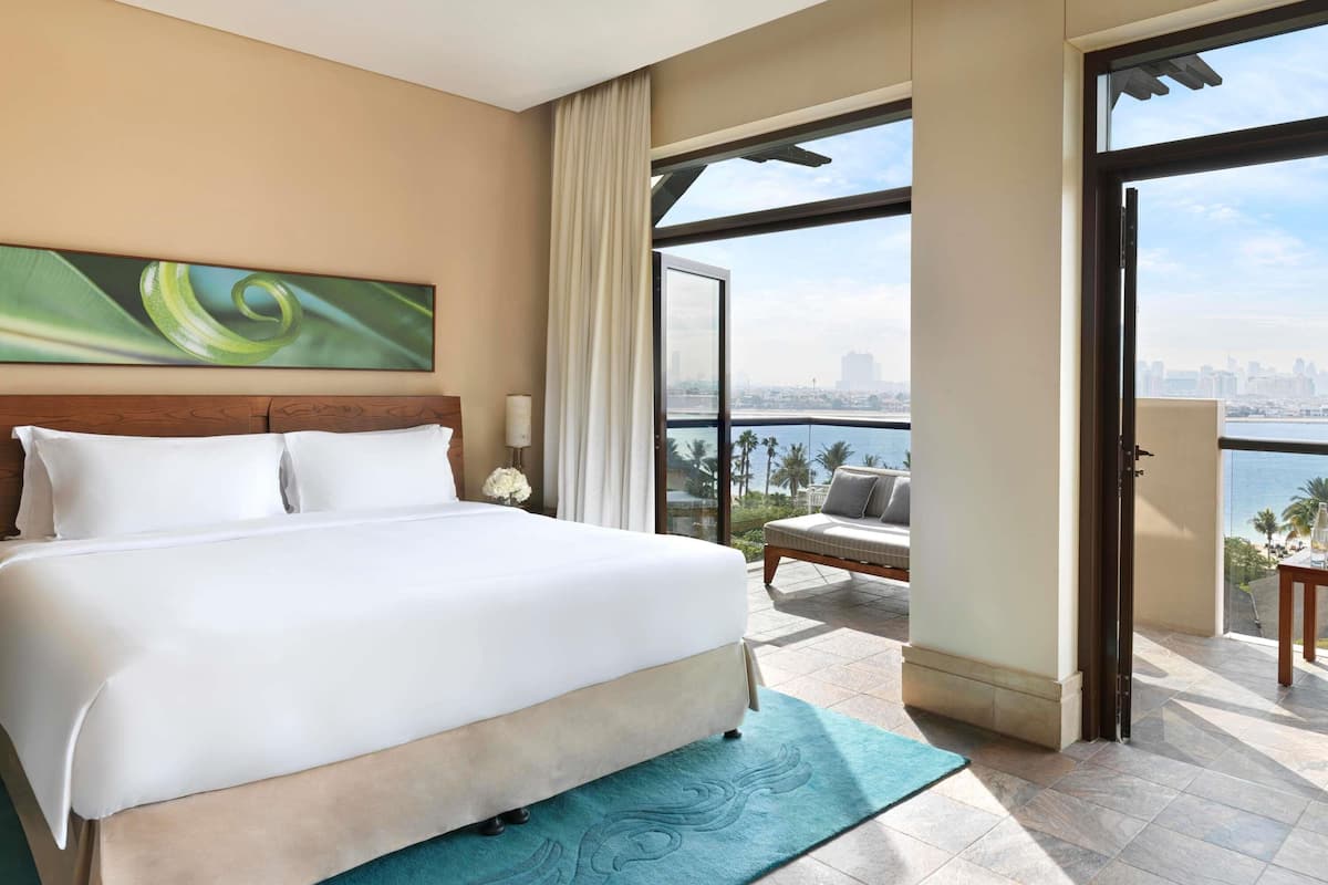 Hotelkamer met een groot bed, uitzicht over de stad en een balkon met een bank.