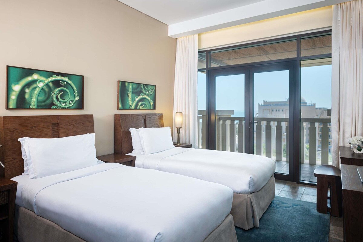 Habitación de hotel con dos camas, un balcón con vistas y obras de arte en las paredes.