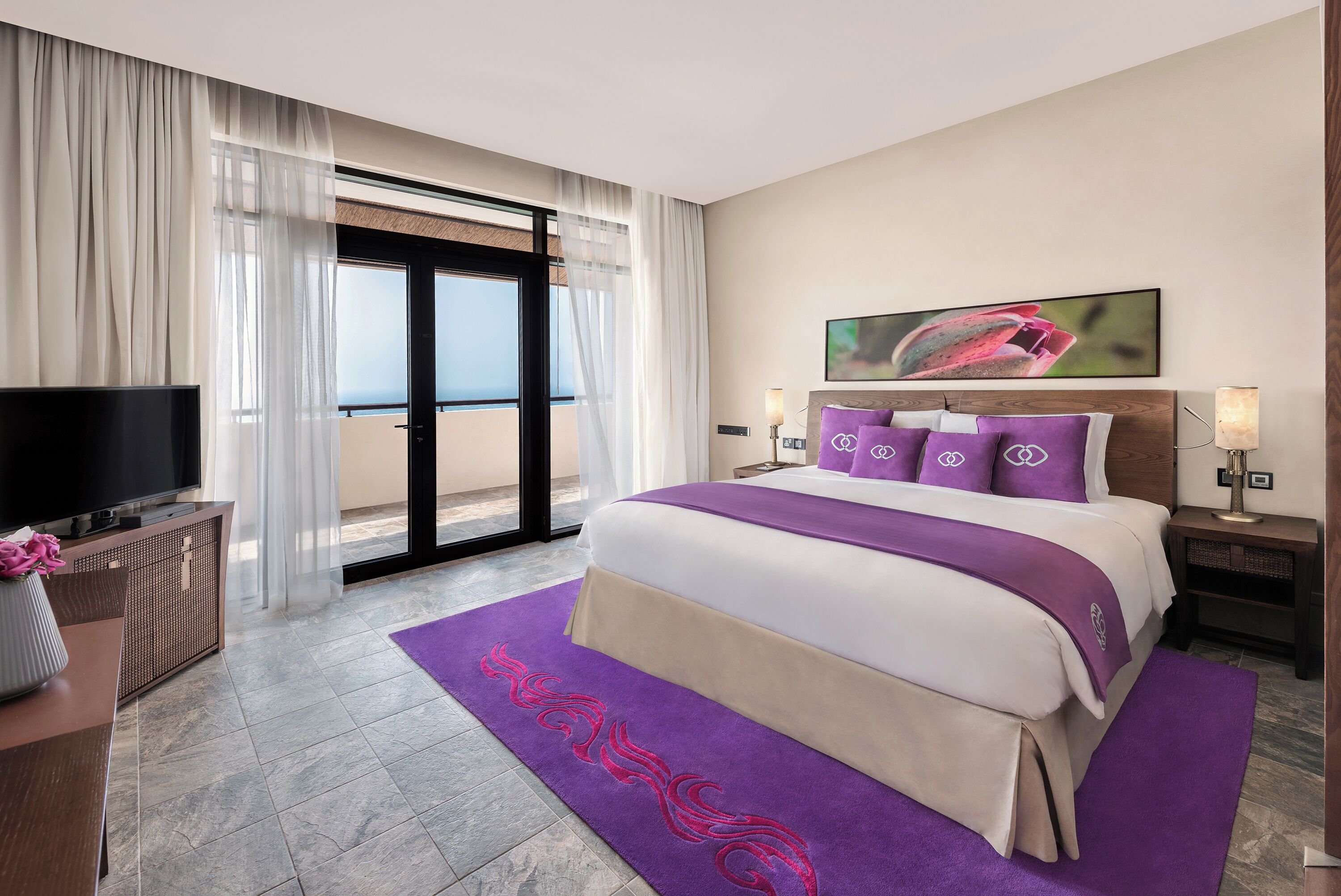 A modern hotel room with a large bed, a TV, and a balcony with a view.