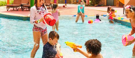 A swimming pool area with multiple people enjoying the water, some holding toys, and others standing or sitting by the poolside.