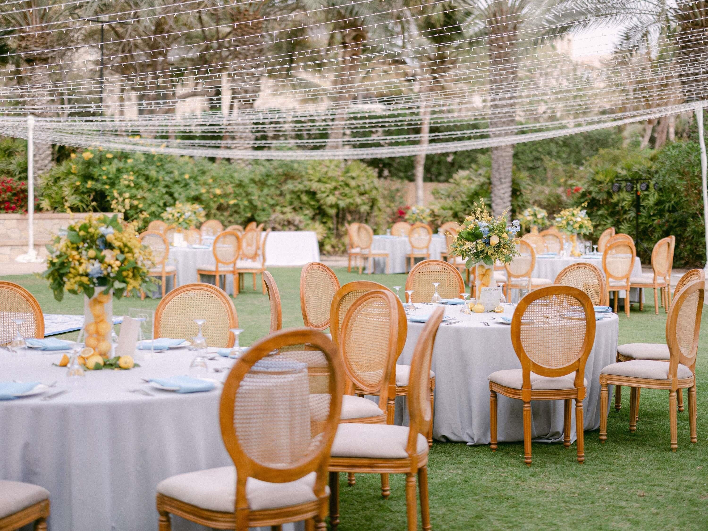 An outdoor event space with round tables, wicker chairs, and string lights.