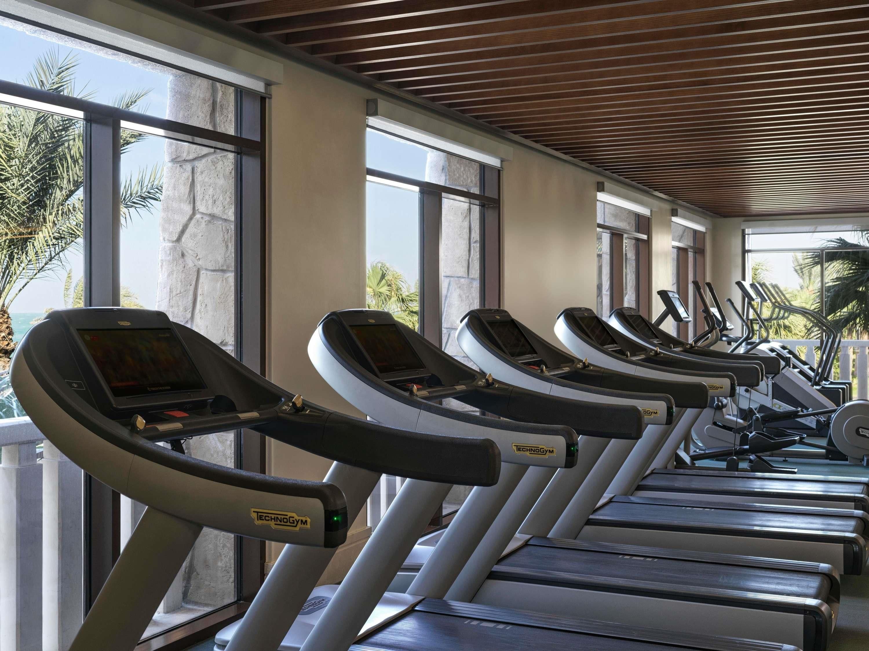 A row of treadmills with digital displays, large windows, and a wooden ceiling.