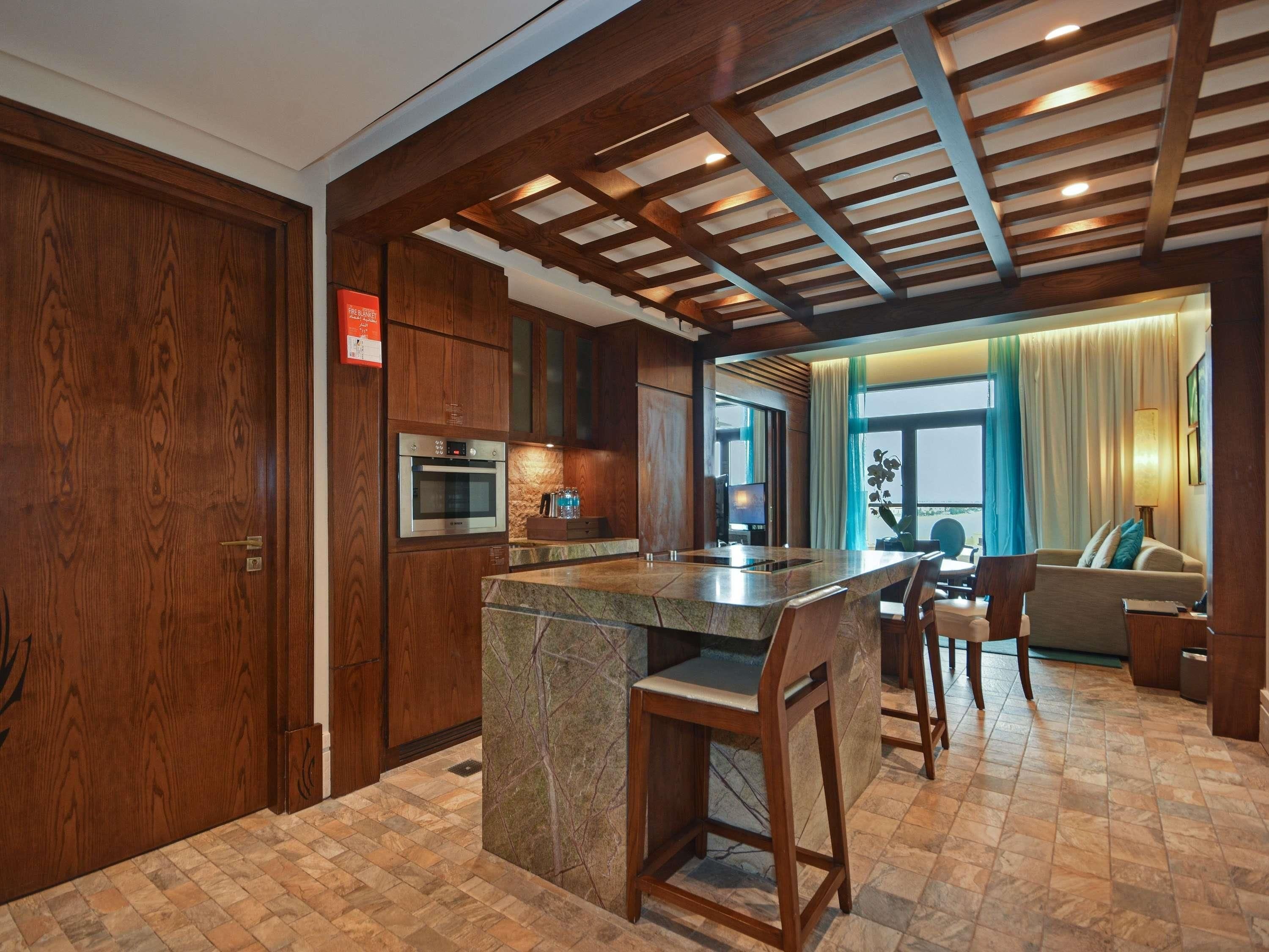 A modern kitchen with wooden cabinets, a built-in oven, and a marble island with bar stools.