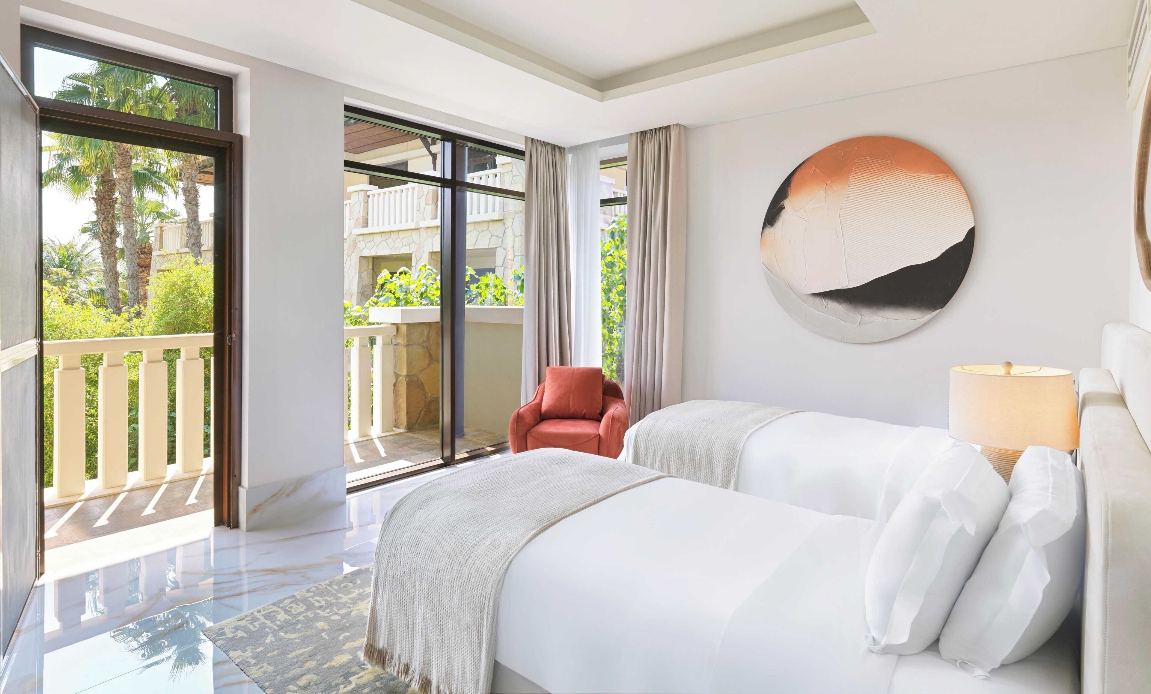 Habitación de hotel con un amplio ventanal corredero que da a un balcón, un espejo redondo en la pared y una cama con ropa blanca.