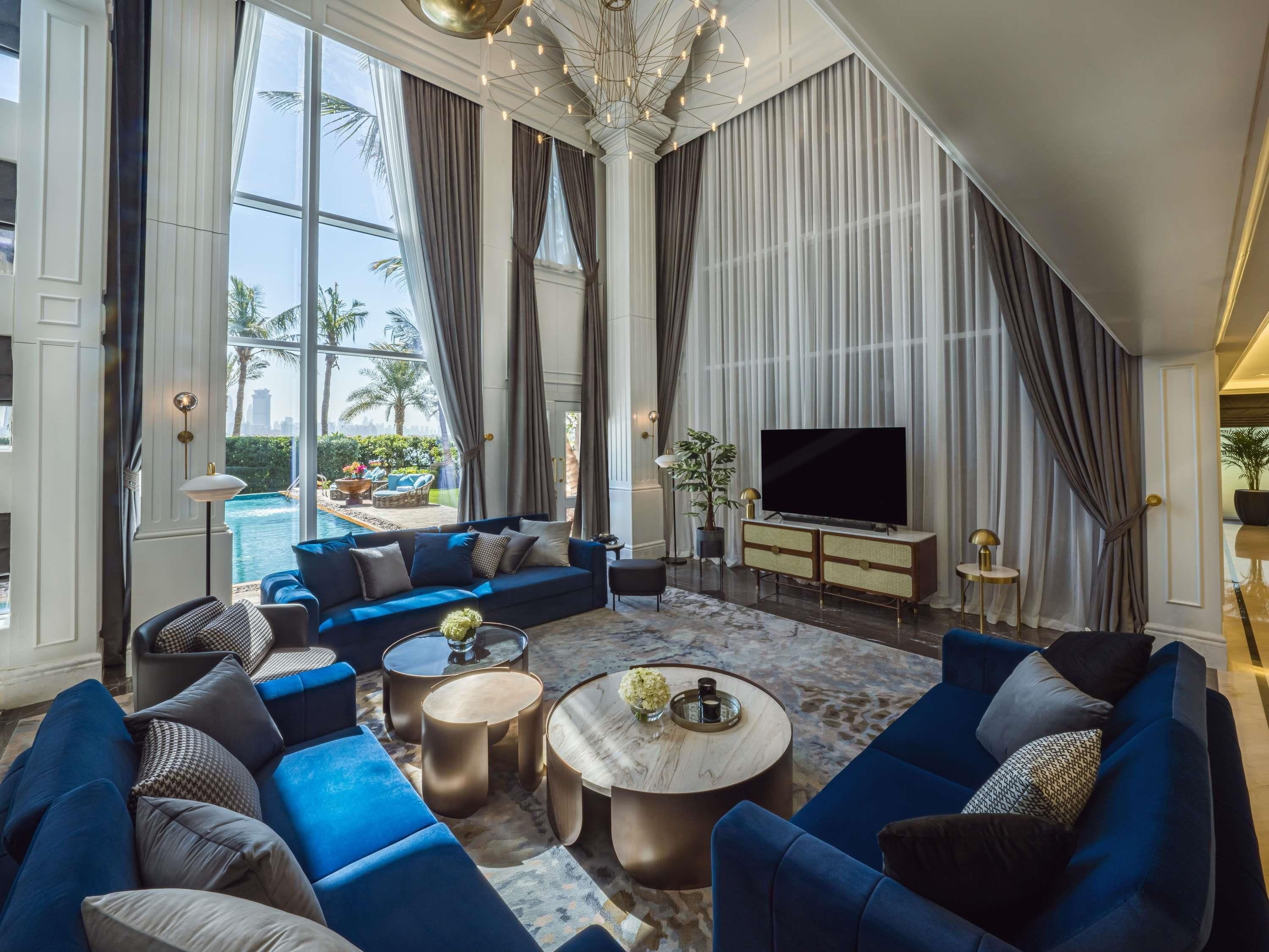 A spacious living room with a large sofa set, a flat-screen TV, and a view of a swimming pool.