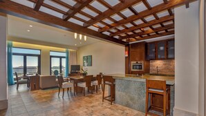 A spacious living area with a wooden ceiling, a kitchen with a stone countertop, and a dining area with chairs and a table.