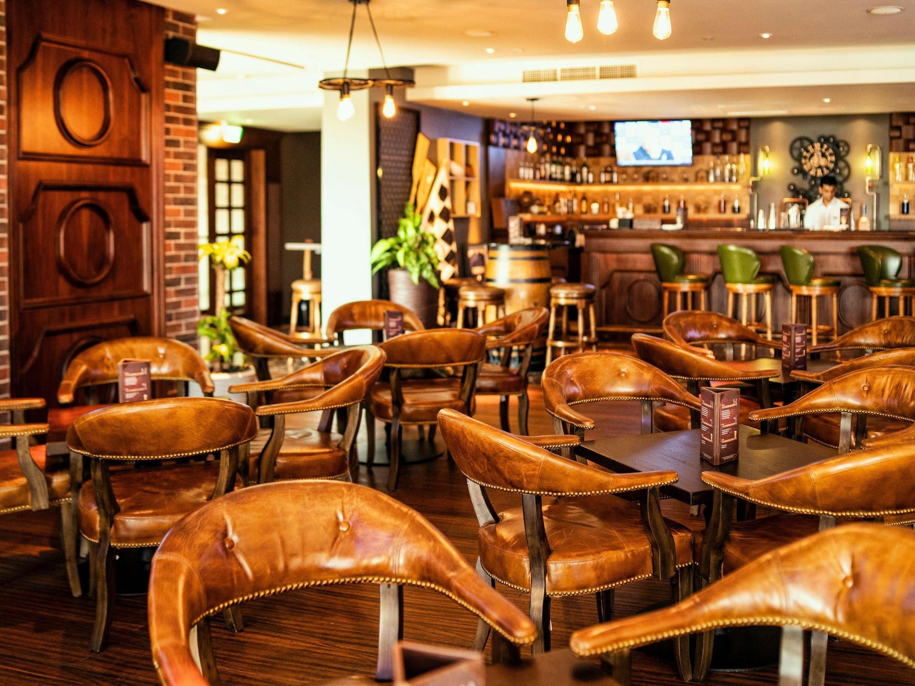 A restaurant interior with leather chairs, wooden tables, a bar area, and a television screen.