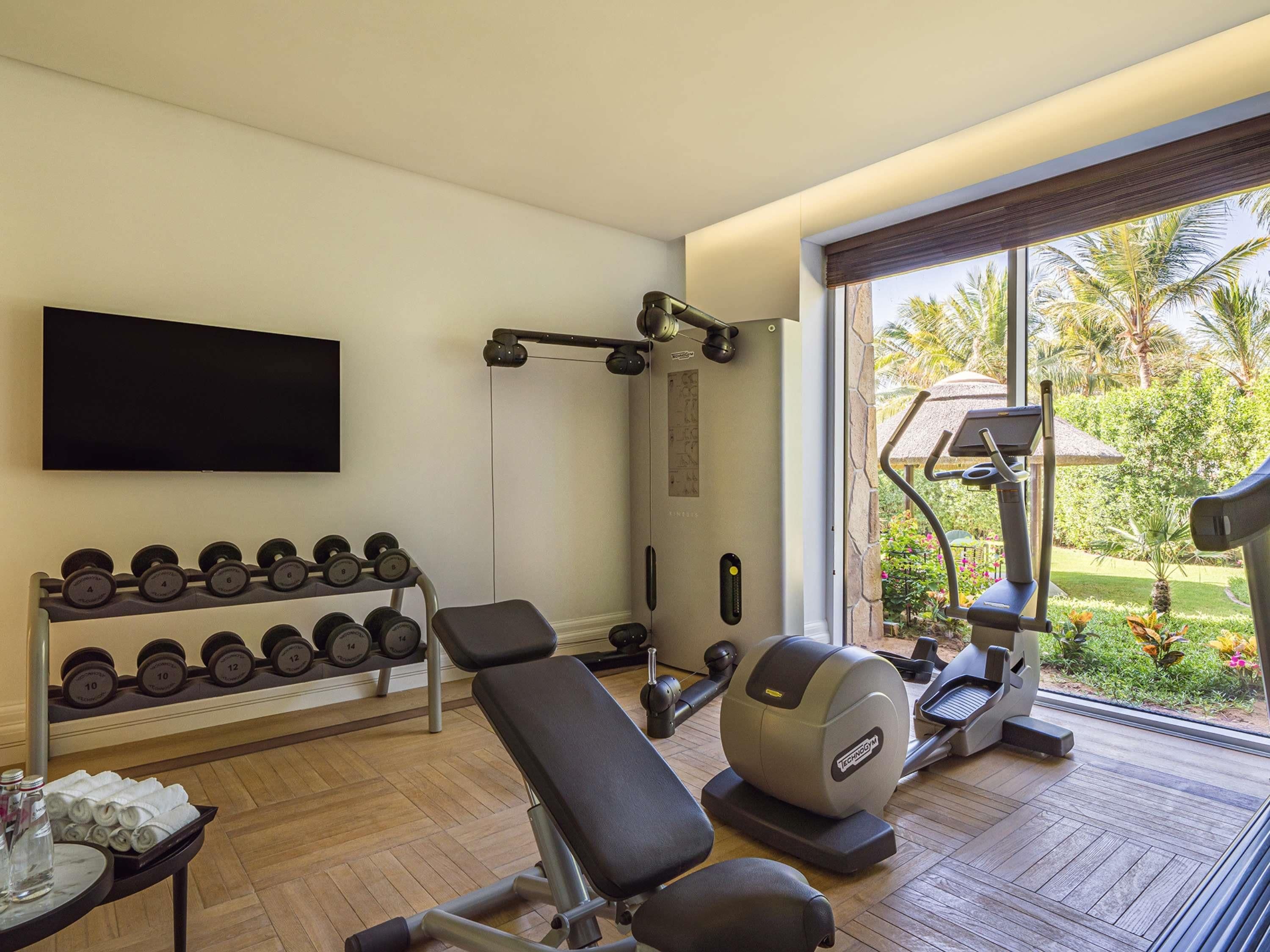 Une salle de sport équipée d’un banc, d’haltères, d’un support à squats et d’un appareil elliptique.