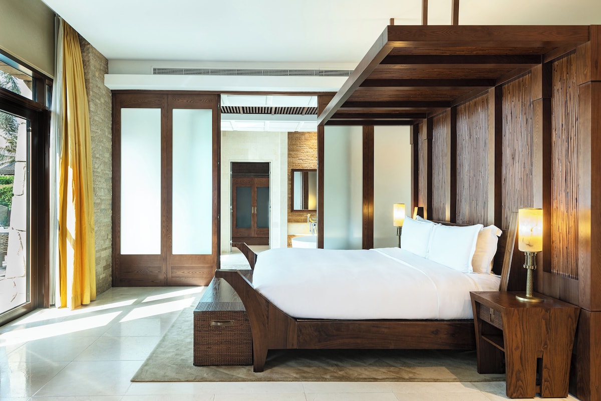A modern bedroom with a large bed, wooden headboard, and a nightstand with a lamp.