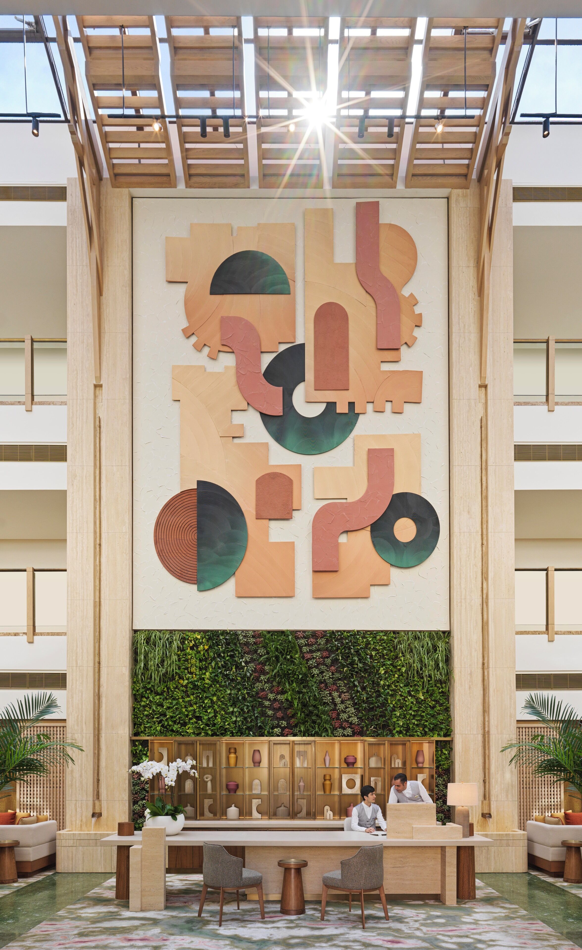 Een lobby met een geometrisch kunstwerk aan de muur, een receptiebalie, een zithoek en een groene wand met planten.