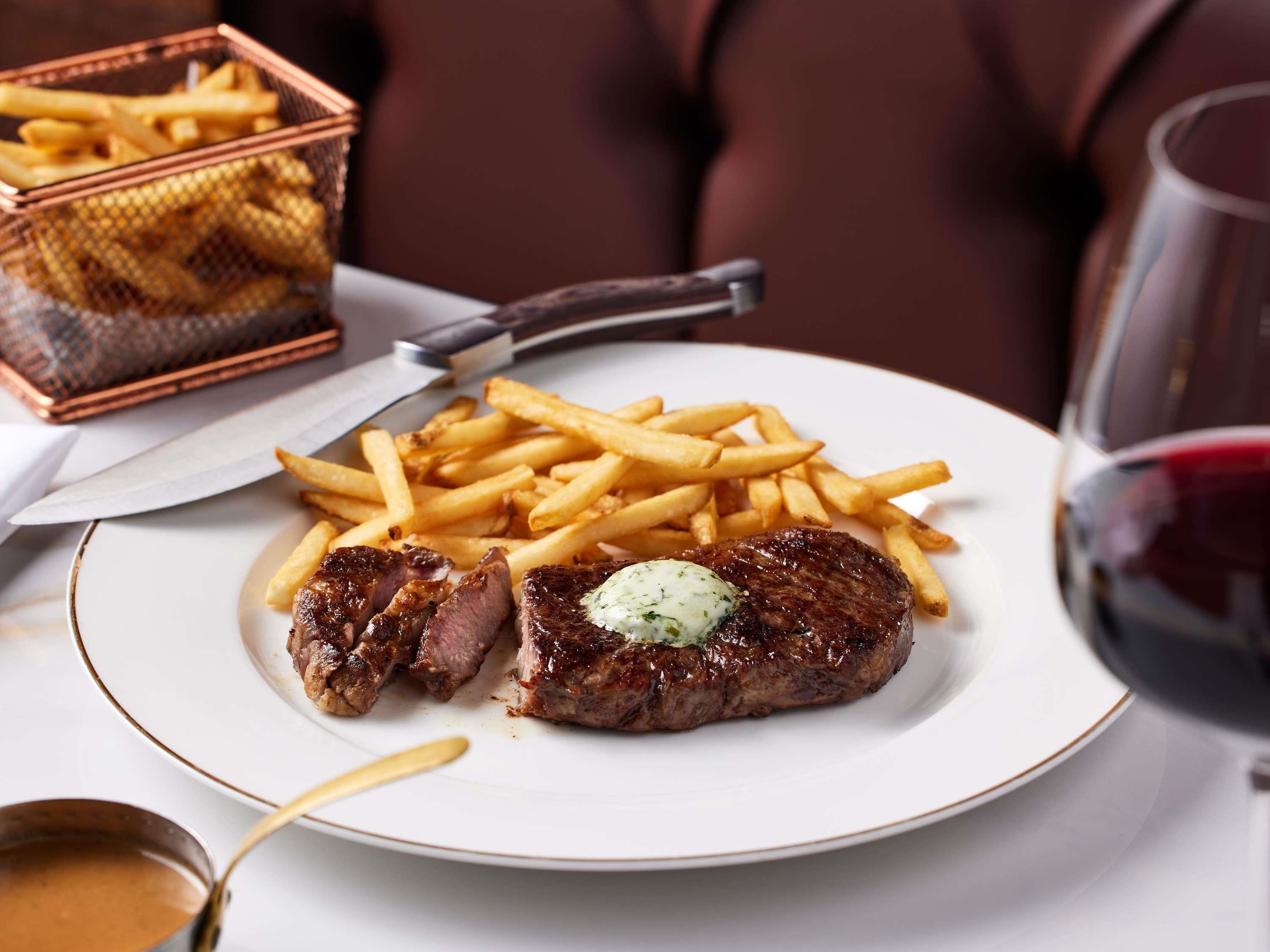 Un plato con bistec y papas fritas, un cuchillo y una copa de vino tinto.