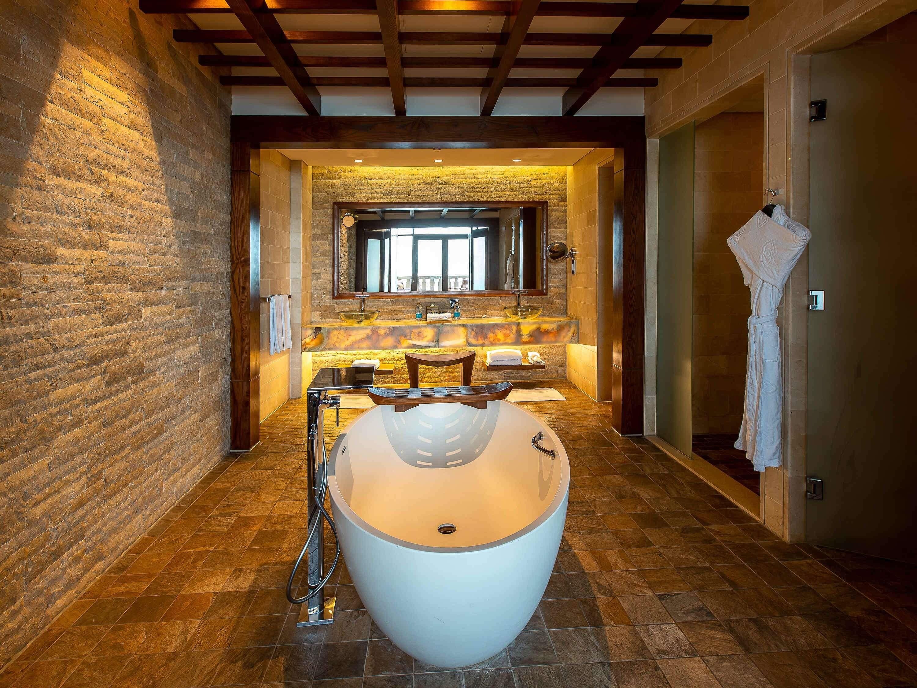 A modern bathroom with a large bathtub, a stone wall, and a wooden ceiling.