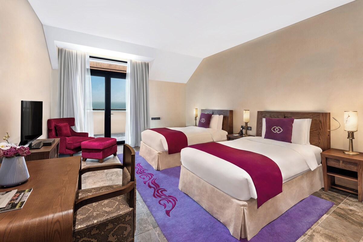 A hotel room with two beds, a desk, a TV, and a red chair.