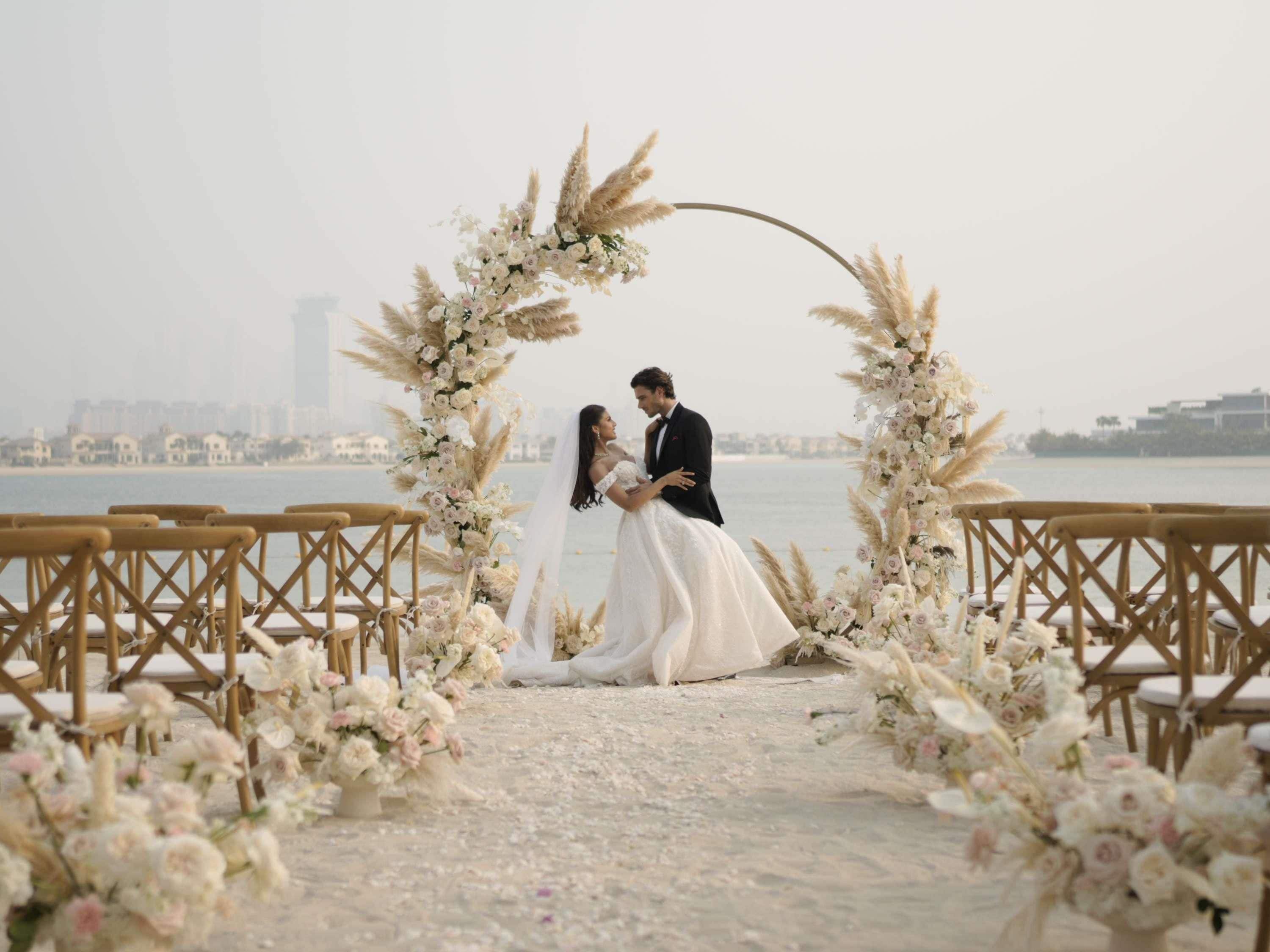 A wedding ceremony with a floral arch and chairs.