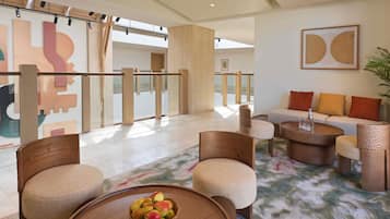 A modern lobby with a seating area, a coffee table with fruit, and a large abstract painting on the wall.