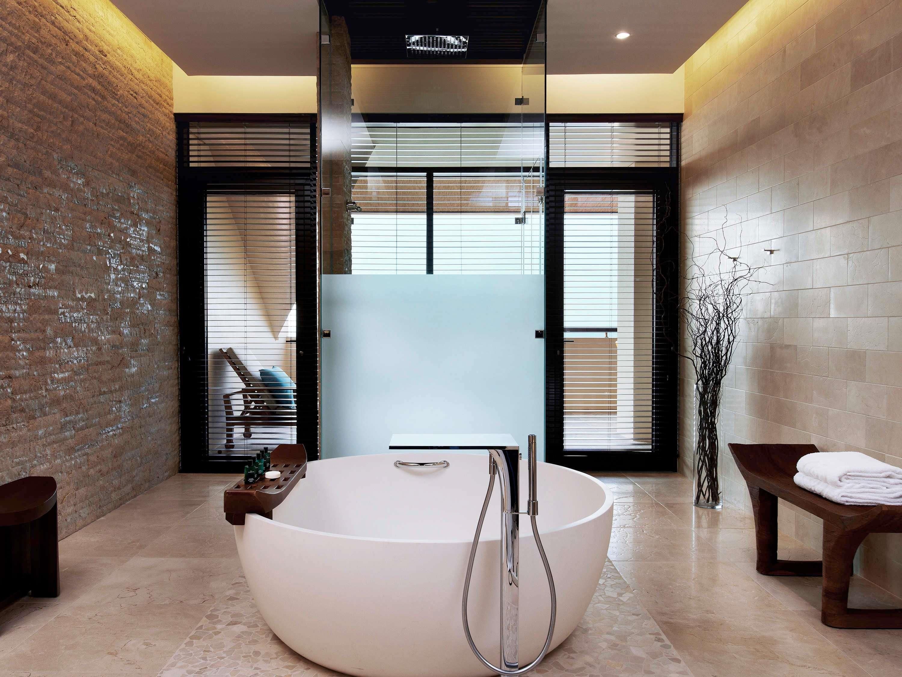 Ein modernes Badezimmer mit einer großen, freistehenden Badewanne, einer Sitzbank und einer Glastür, die auf einen Balkon führt.