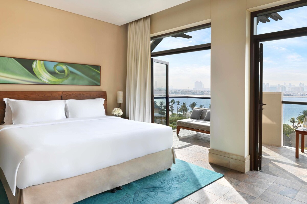 Hotelkamer met een groot bed, uitzicht over de stad en een balkon met een bank.
