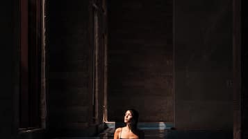 A person in a dimly lit indoor pool with stone walls and large windows.
