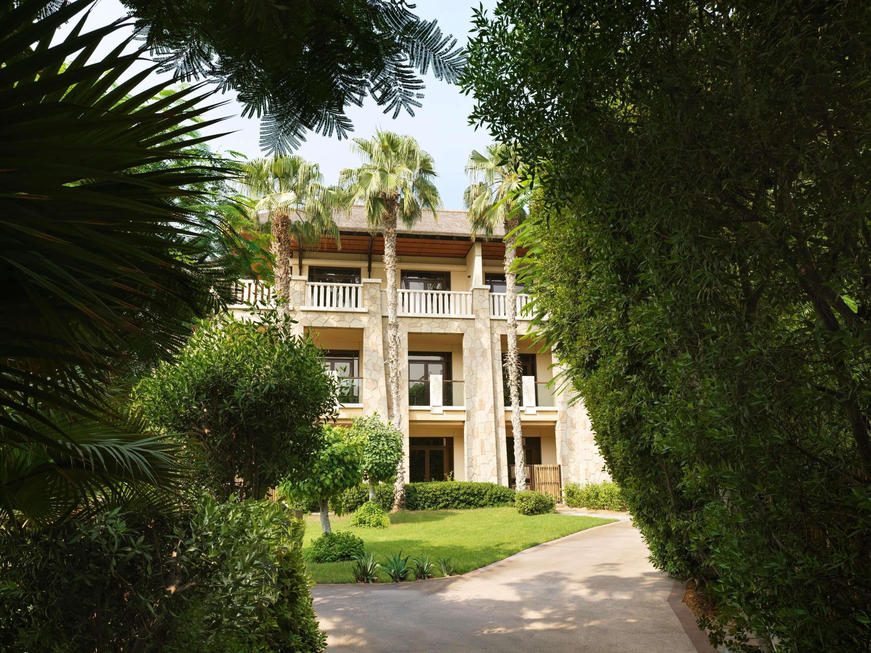 A multi-story hotel with a stone facade, balconies, and a well-maintained garden.