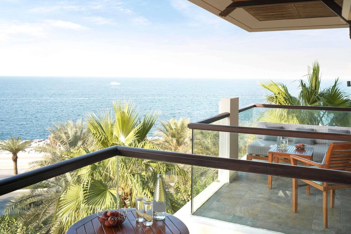 Een balkon met uitzicht op zee, voorzien van een tafel en stoelen, en een glazen balustrade.