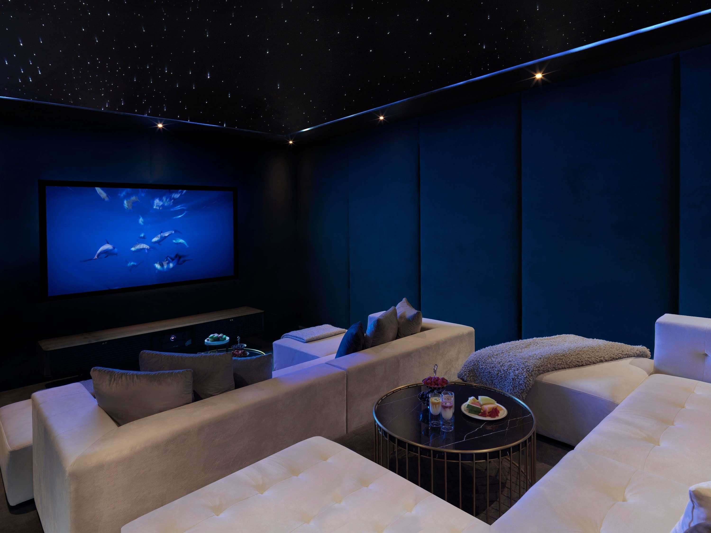 A dark room with a large screen, comfortable seating, and a small table with snacks.