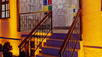 Una escalera conduce a una entrada luminosa con una puerta de cristal decorativa y barandilla de metal.