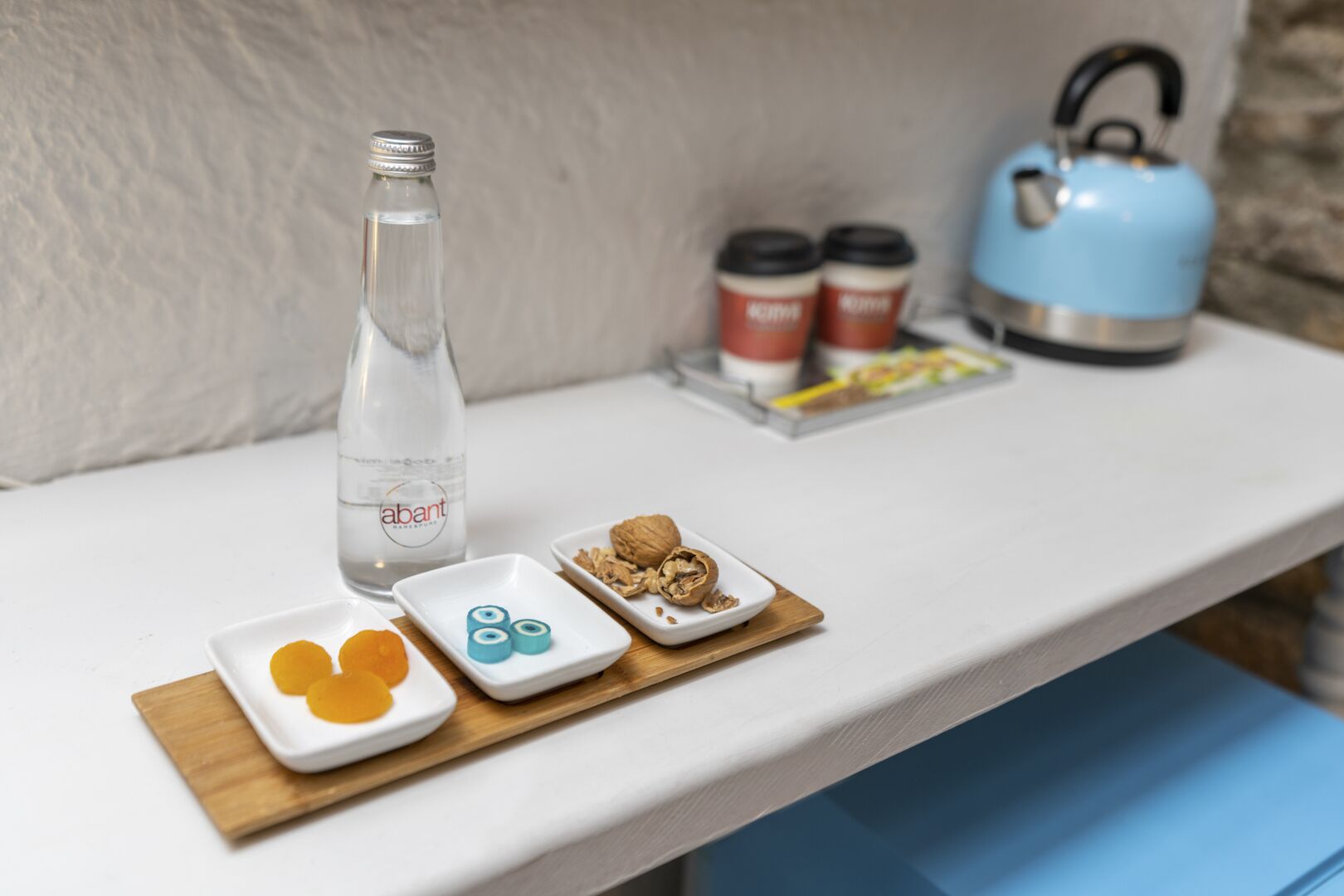 Une table avec une bouteille d’eau, deux tasses à café, une bouilloire bleue et de petites assiettes contenant des aliments.