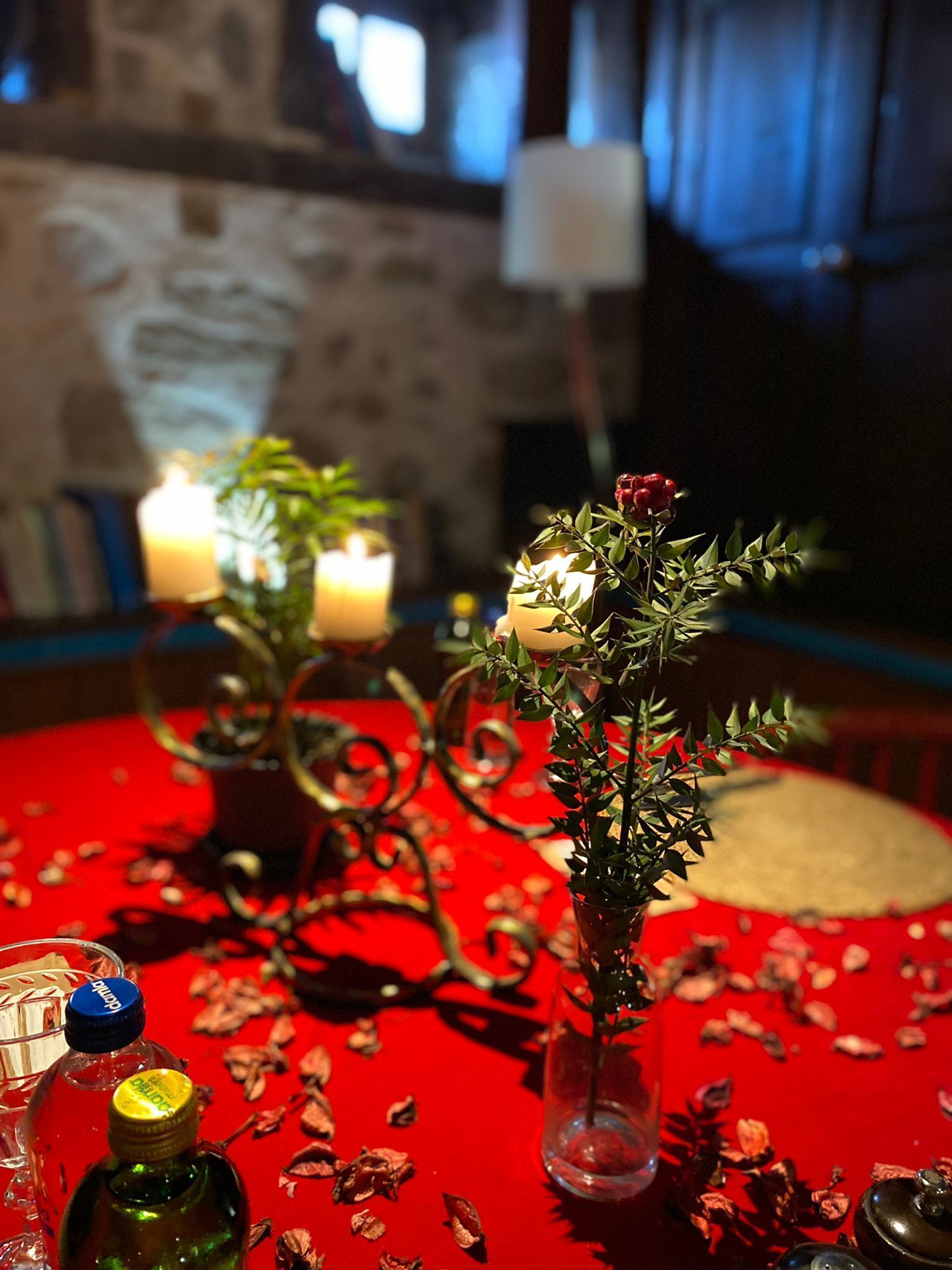 A table with candles, a potted plant, and scattered rose petals.