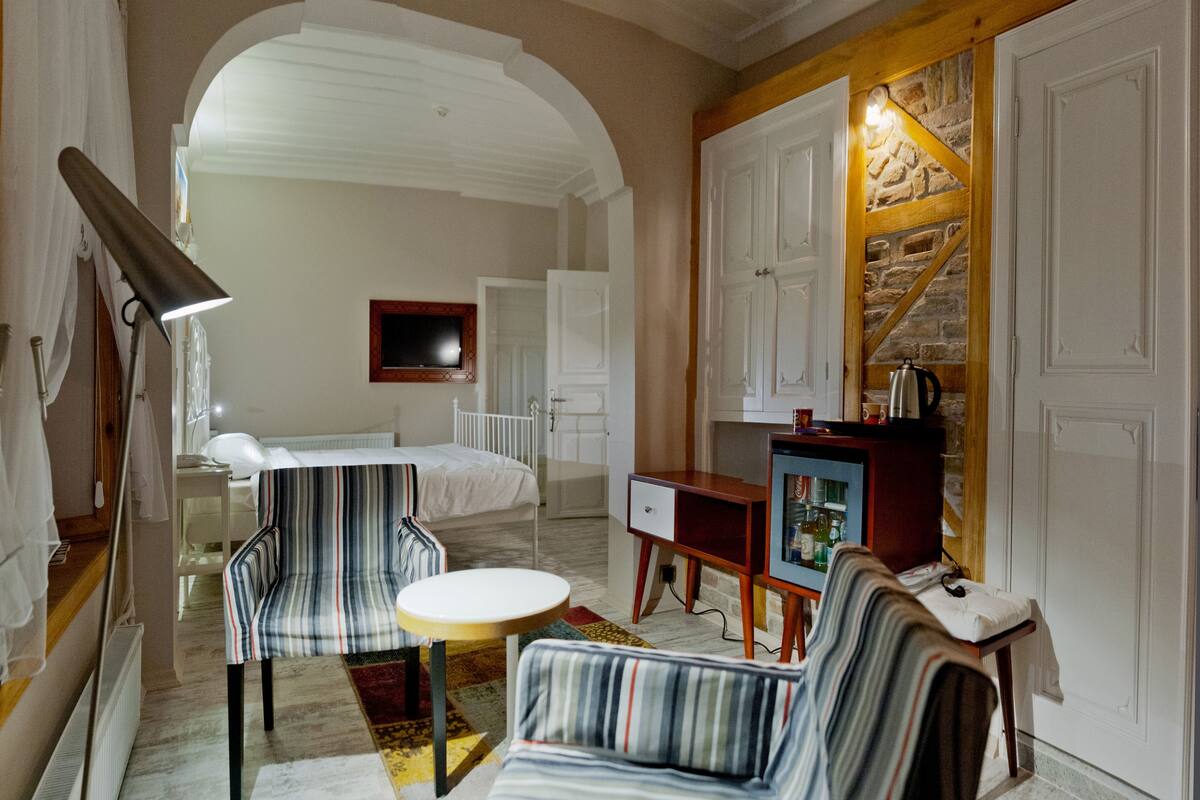 A hotel room with a bed, a sitting area with a table and chairs, a television, and a minibar.