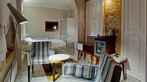 Habitación de hotel con cama, zona de estar con mesa y sillas, televisor y minibar.