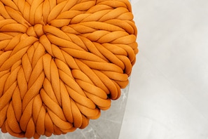 Een ronde, oranje pouf van gebreid materiaal met een structuur.