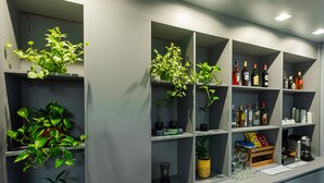 Un espace bar doté de plusieurs étagères où sont disposées des plantes, des bouteilles et des verres.