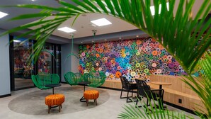 Un espace de bureau moderne avec des chaises vertes et noires, un comptoir d’accueil en bois et un mur coloré orné de motifs circulaires.