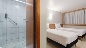 Quarto de hotel com chuveiro, duas camas, uma cabeceira de madeira e um aparelho de iluminação.