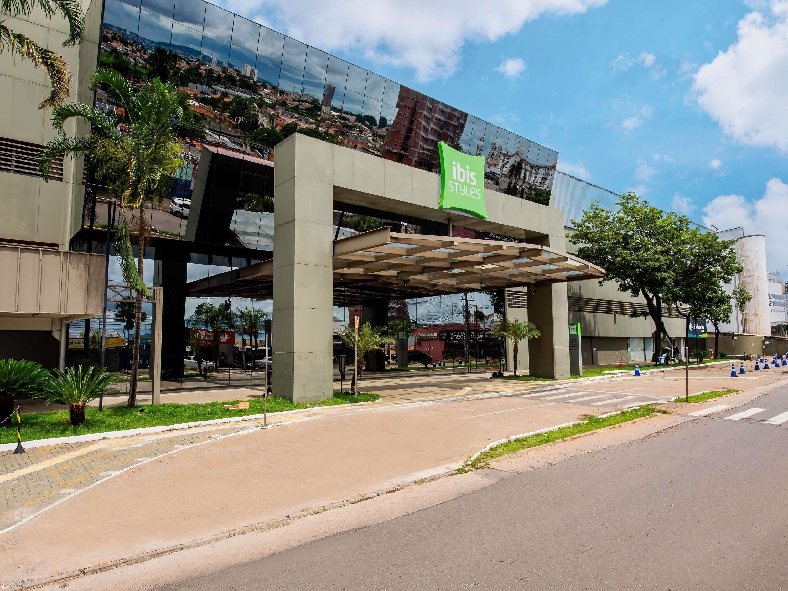 Un edificio moderno con fachada de vidrio, un letrero verde que indica 'ibis Styles' y un área de acceso cubierta.