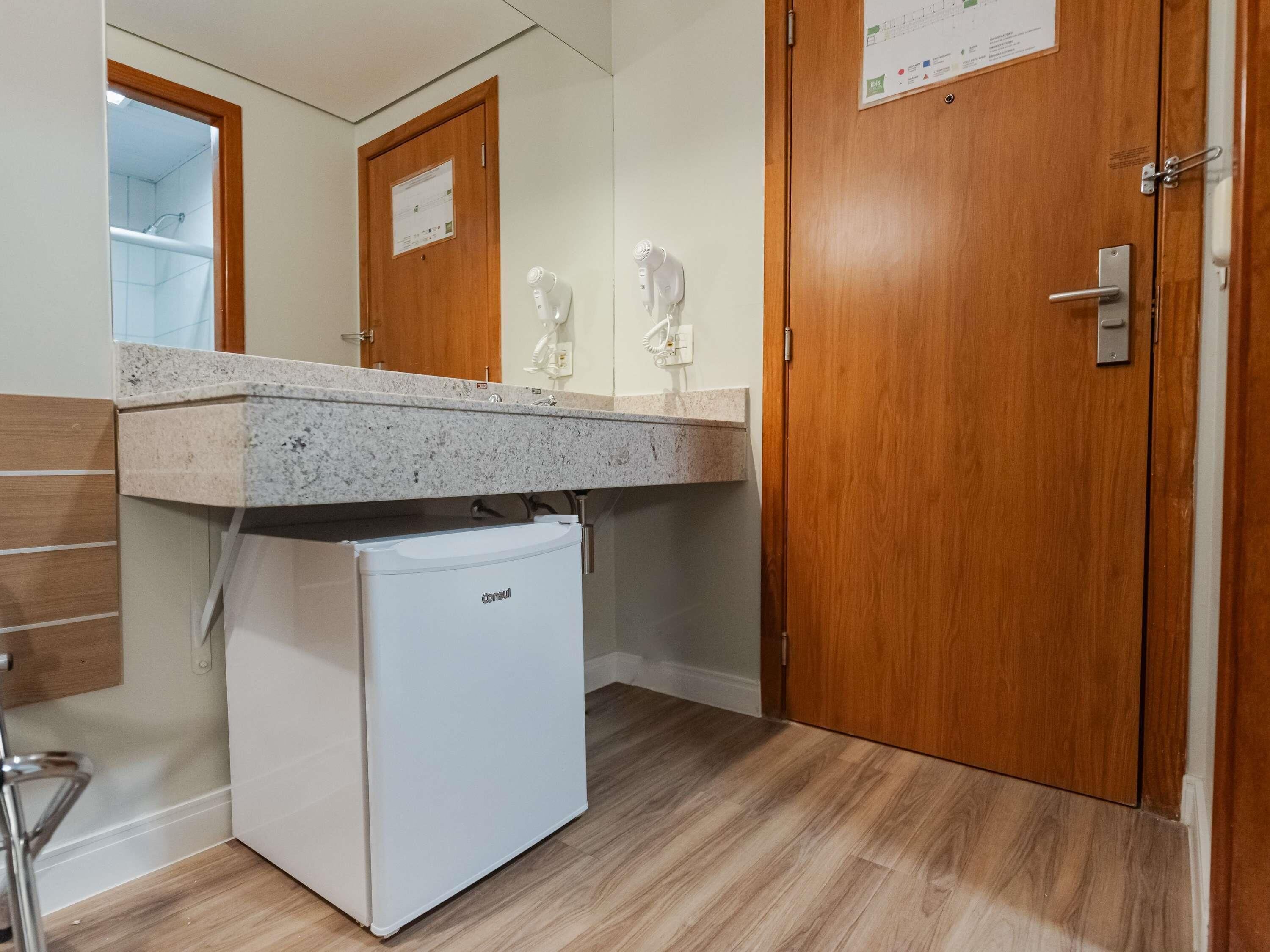 Un bagno compatto con un piccolo frigorifero bianco, una porta in legno e uno specchio.