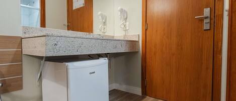 Un bagno compatto con un piccolo frigorifero bianco, una porta in legno e uno specchio.