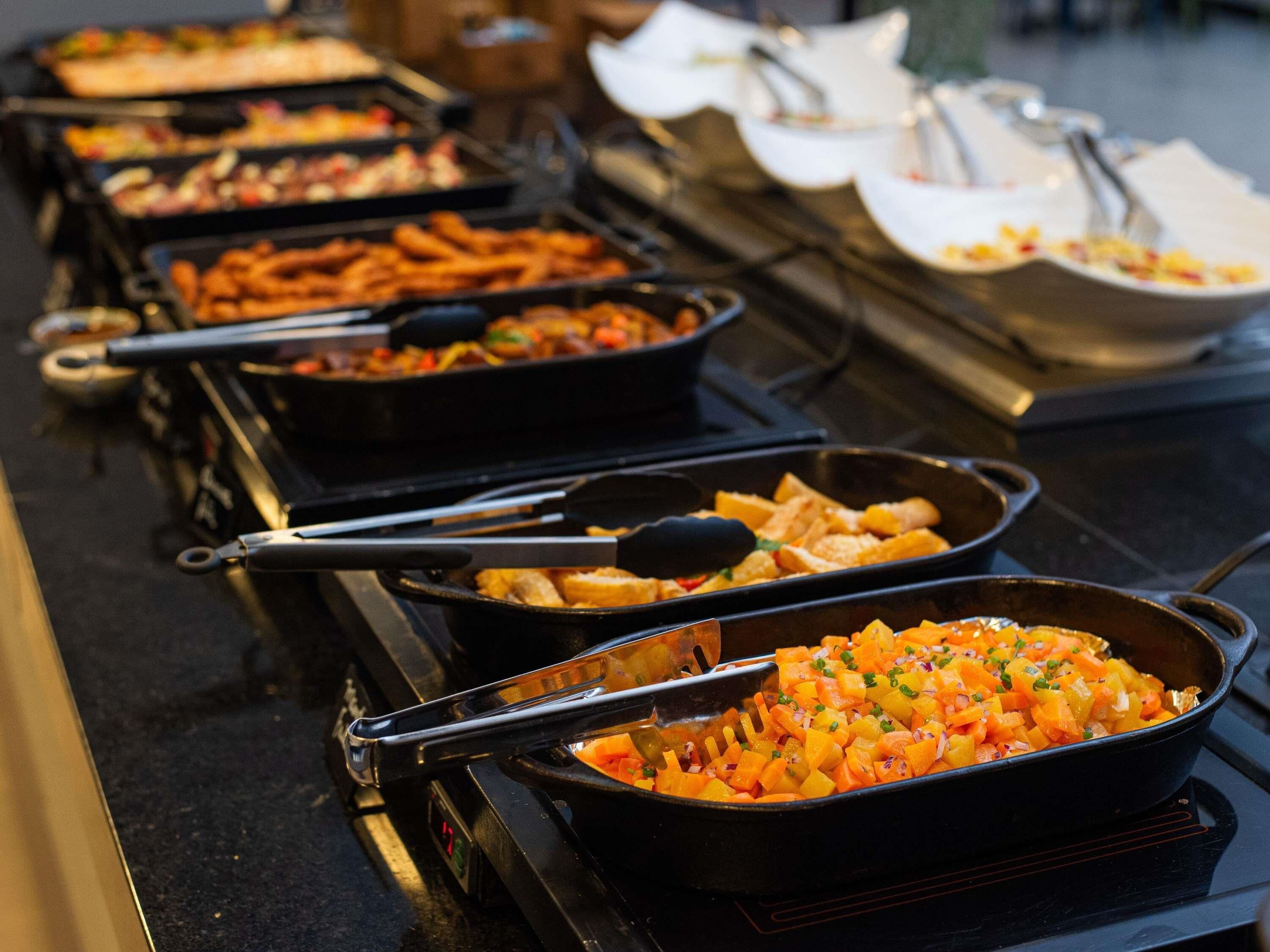 Un buffet proposant divers plats présentés dans des plats noirs, dont un contenant des légumes coupés en dés.