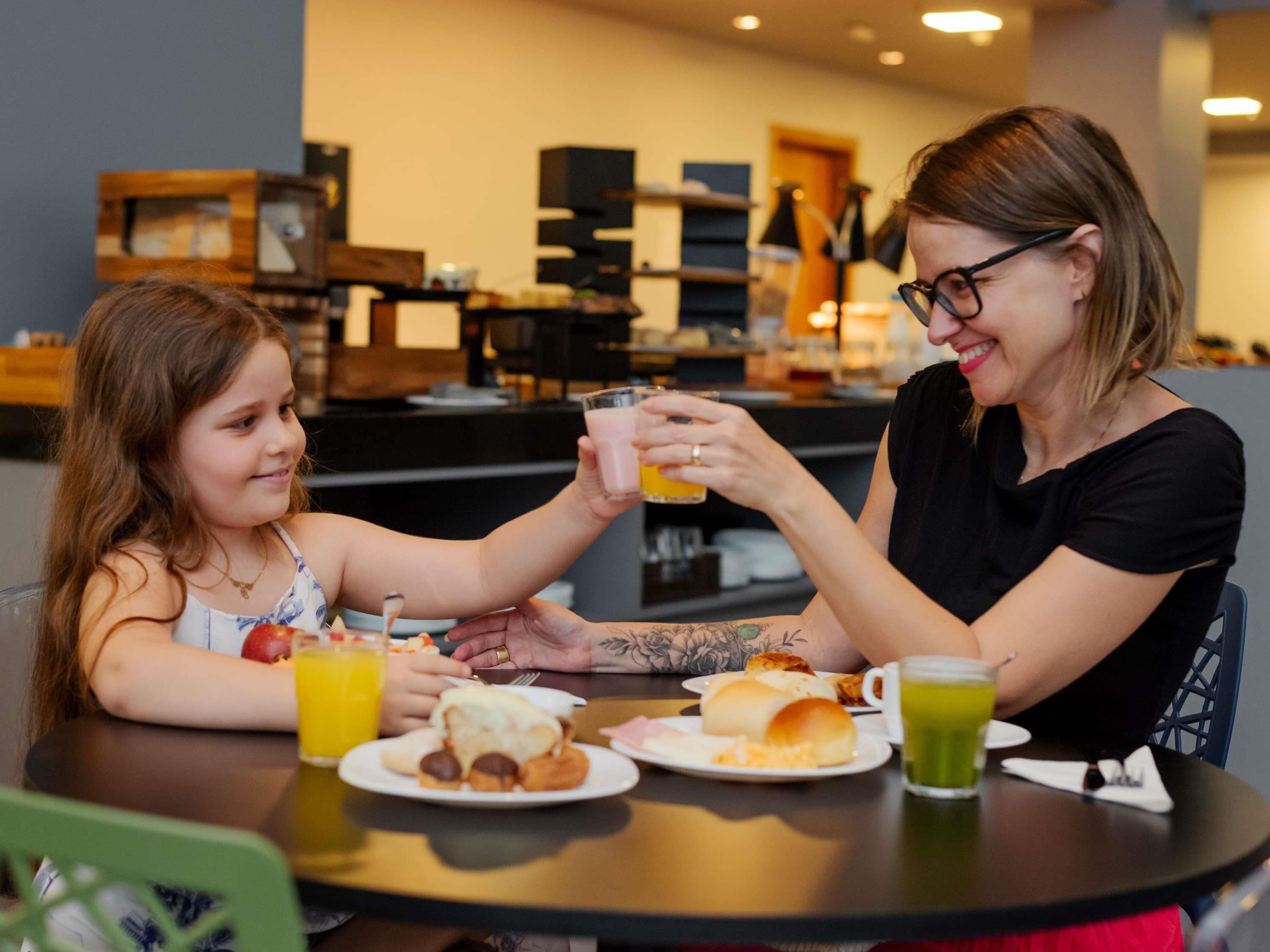 Dos personas sentadas en una mesa redonda con comida y bebidas, en un café con una barra y estanterías al fondo.